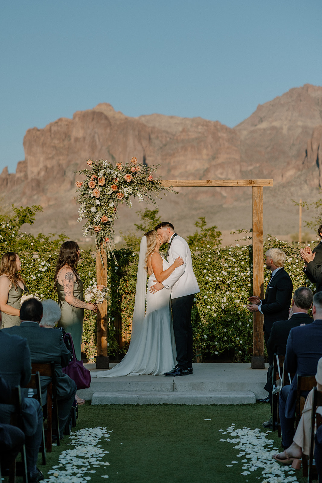 Bride and groom sharing their first kiss under a floral arch with mountain views at one of Arizona’s most iconic wedding venues.