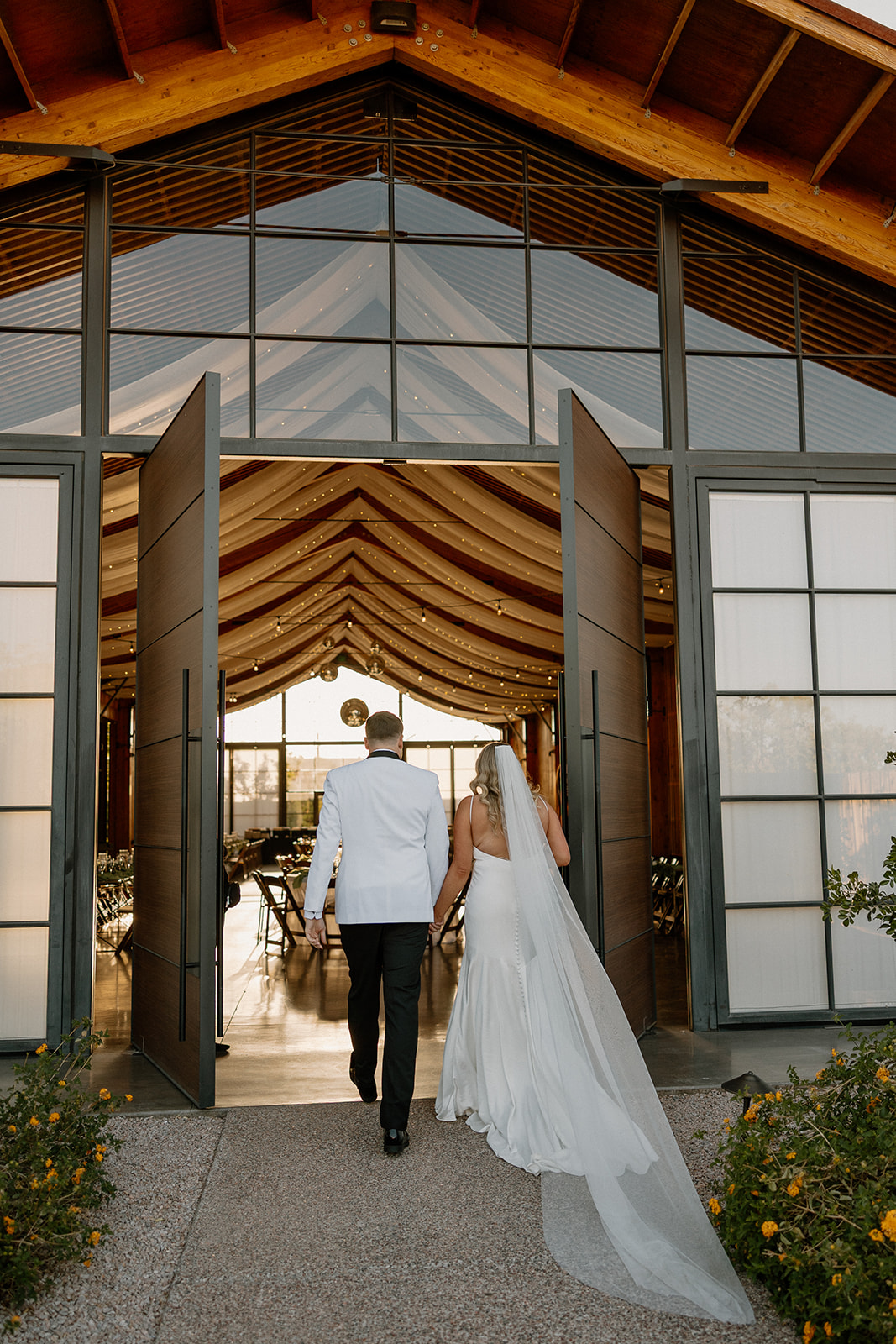 Couple walking into their wedding reception hand-in-hand through open barn doors, just as golden hour hits.