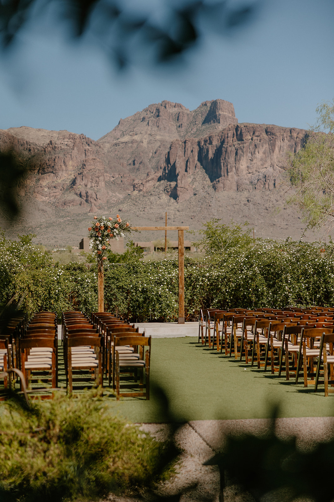 Wedding ceremony space framed by wooden chairs, a floral arch, and the dramatic Superstition Mountains in the distance.