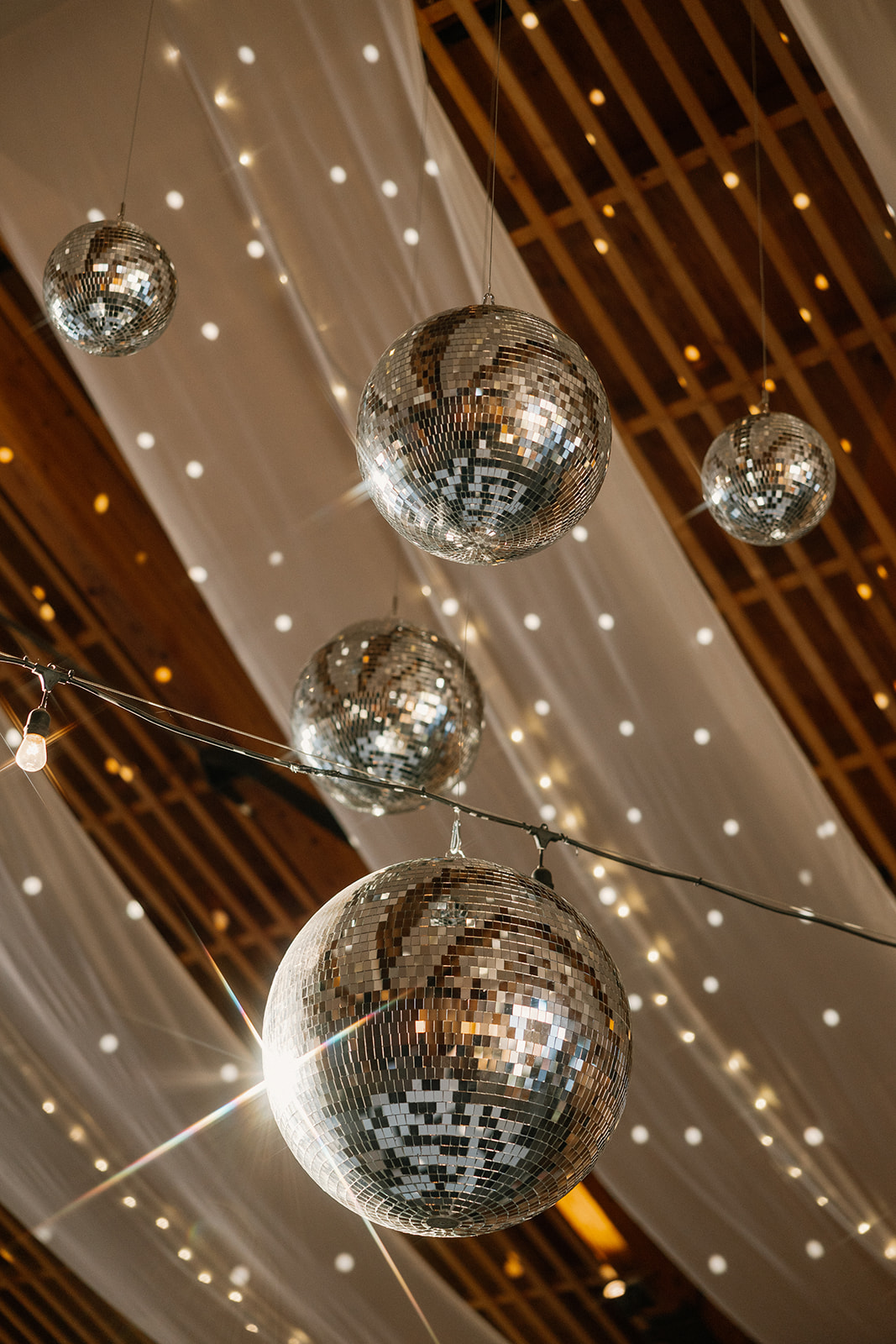 Close-up of disco balls hanging from a draped wooden ceiling, reflecting lights inside one of the boldest wedding venues in Arizona.
