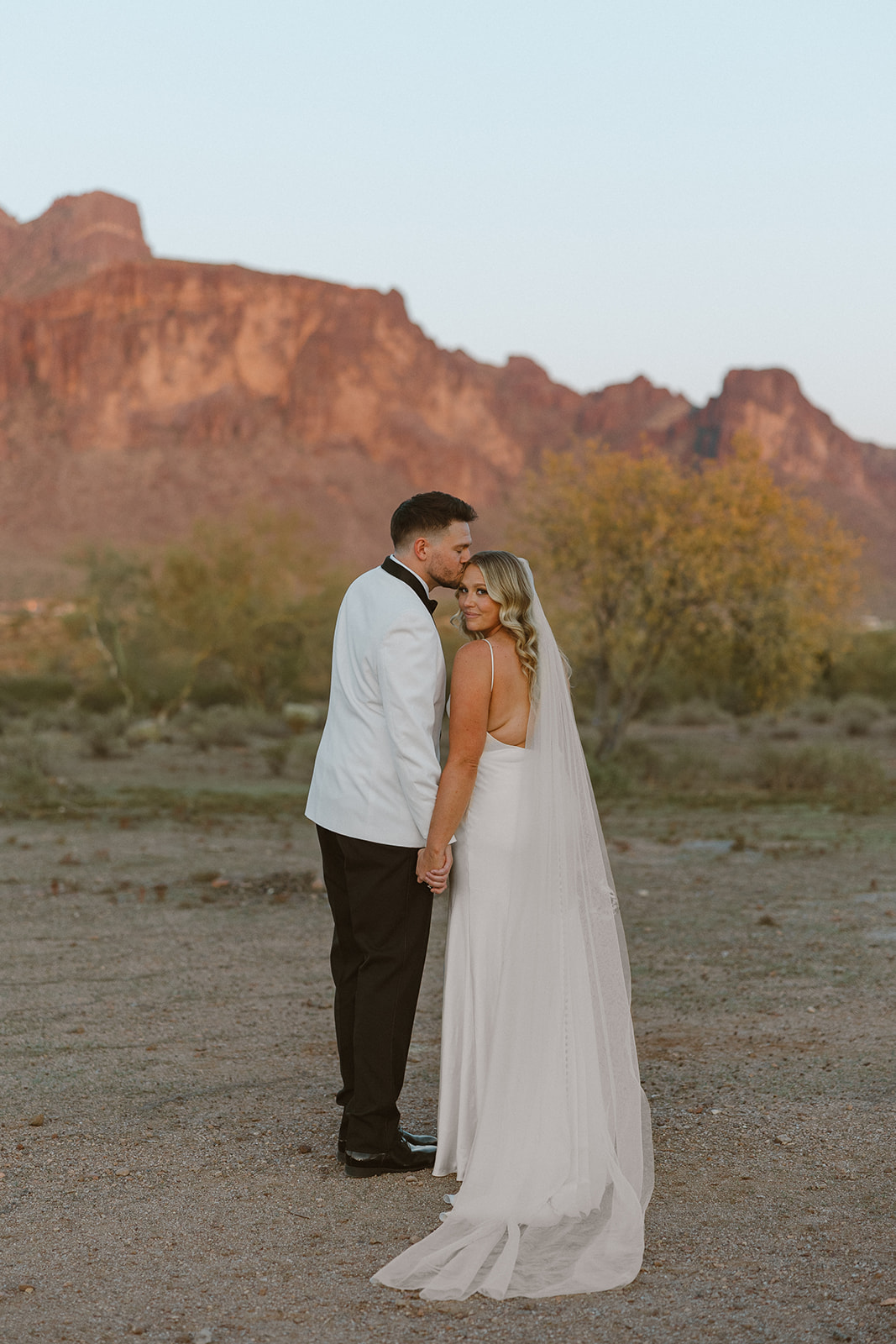 Couple sharing an intimate moment during golden hour with rugged desert mountains in the background at a wedding venue in Arizona.