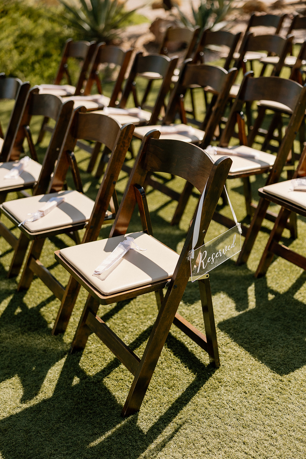 Close-up of reserved ceremony chairs with white ribbons and personalized signage on a grassy aisle.