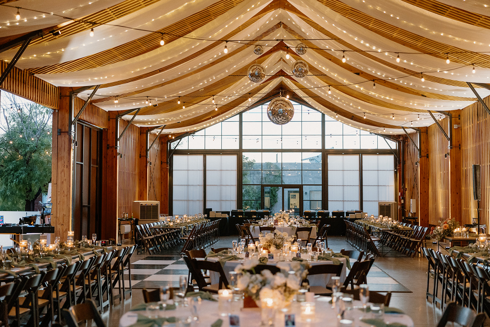 Candlelit reception setup with long wooden tables, disco balls, and sheer drapery at an indoor desert wedding venue in Arizona.