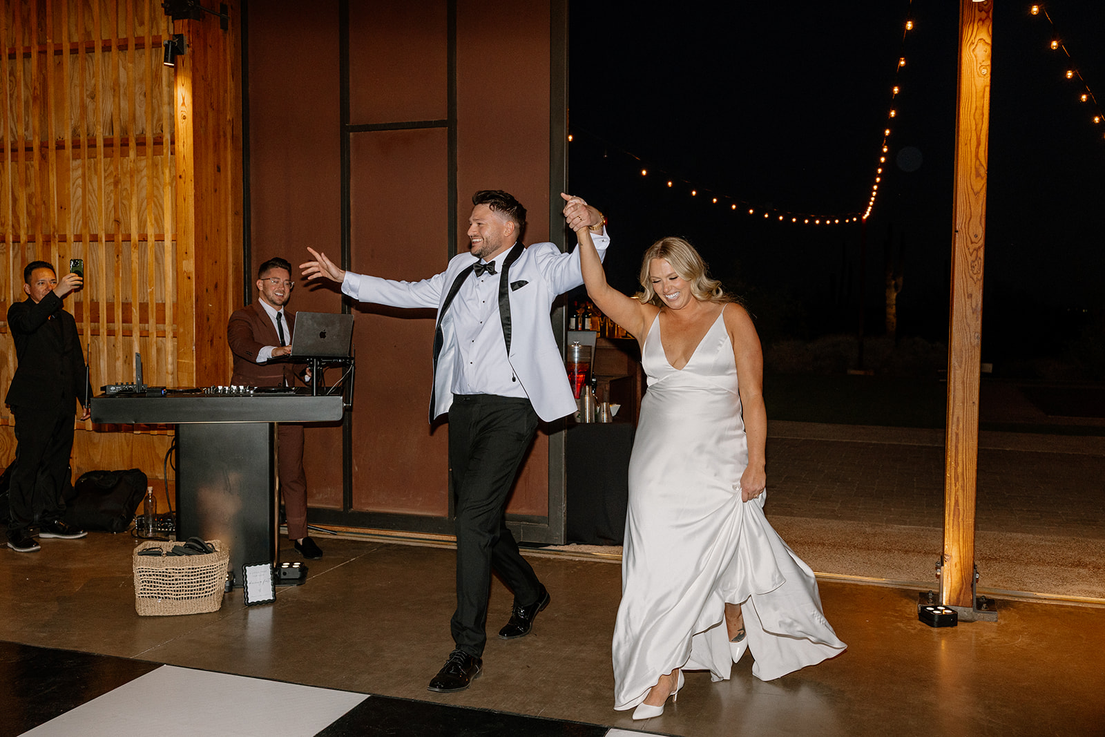 Bride and groom make their grand entrance into the reception, lit by string lights and surrounded by cheers.