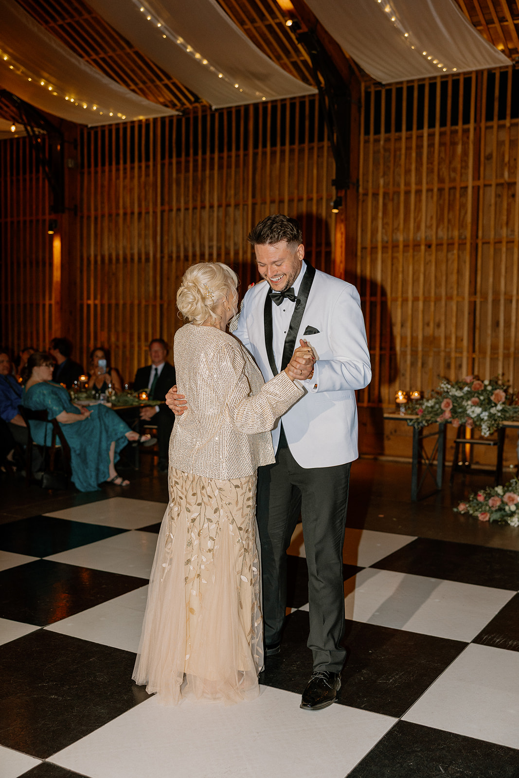 Groom dancing with his mother during the reception, both smiling as guests look on in the background.