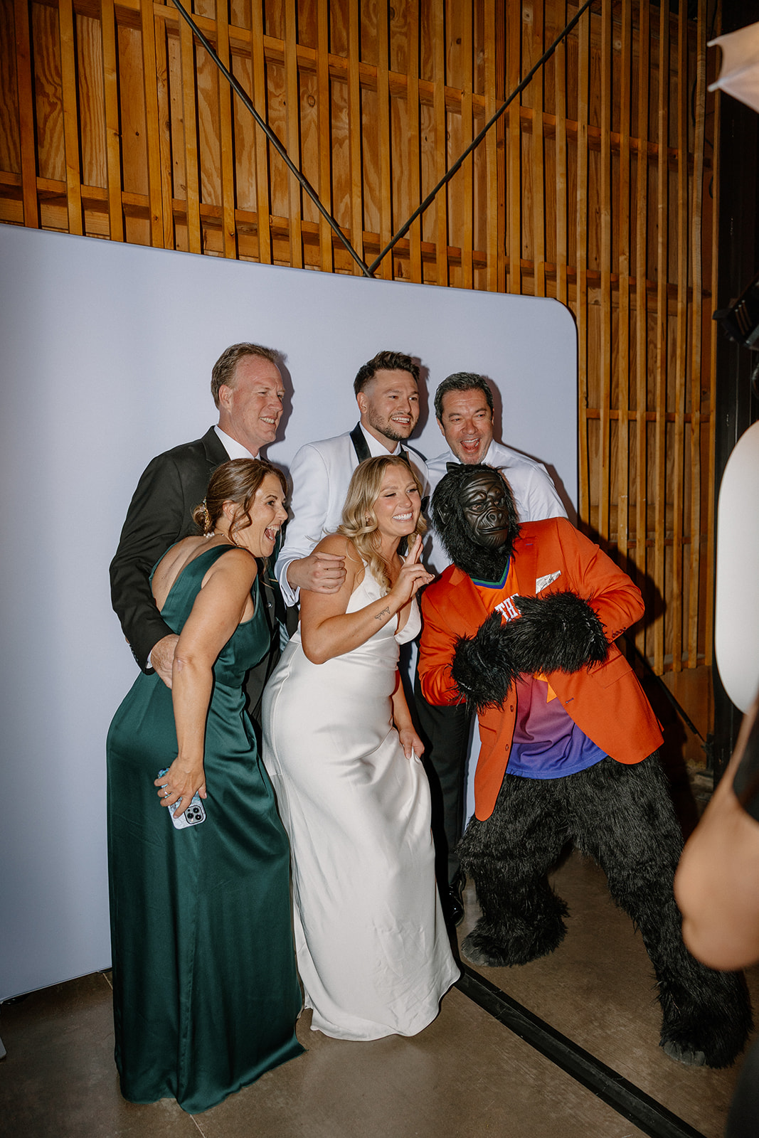 Bride and groom pose with family and the Suns Gorilla mascot in front of a photo backdrop during their lively Arizona wedding.