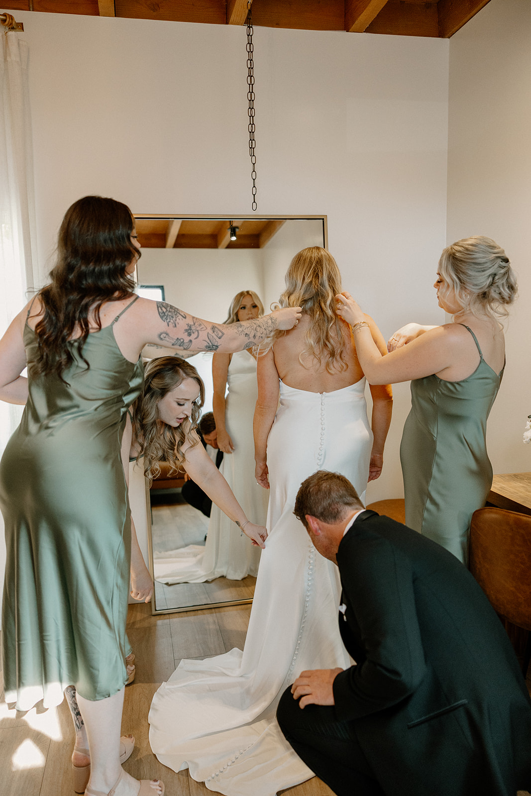Bridesmaids and a groomsman help the bride into her dress, adjusting every detail before the ceremony begins.