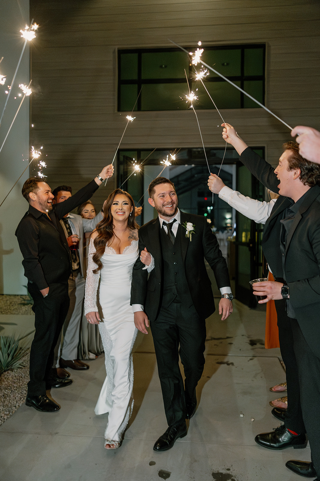 Bride and groom joyfully walk through a sparkler tunnel, surrounded by friends celebrating under the night sky.