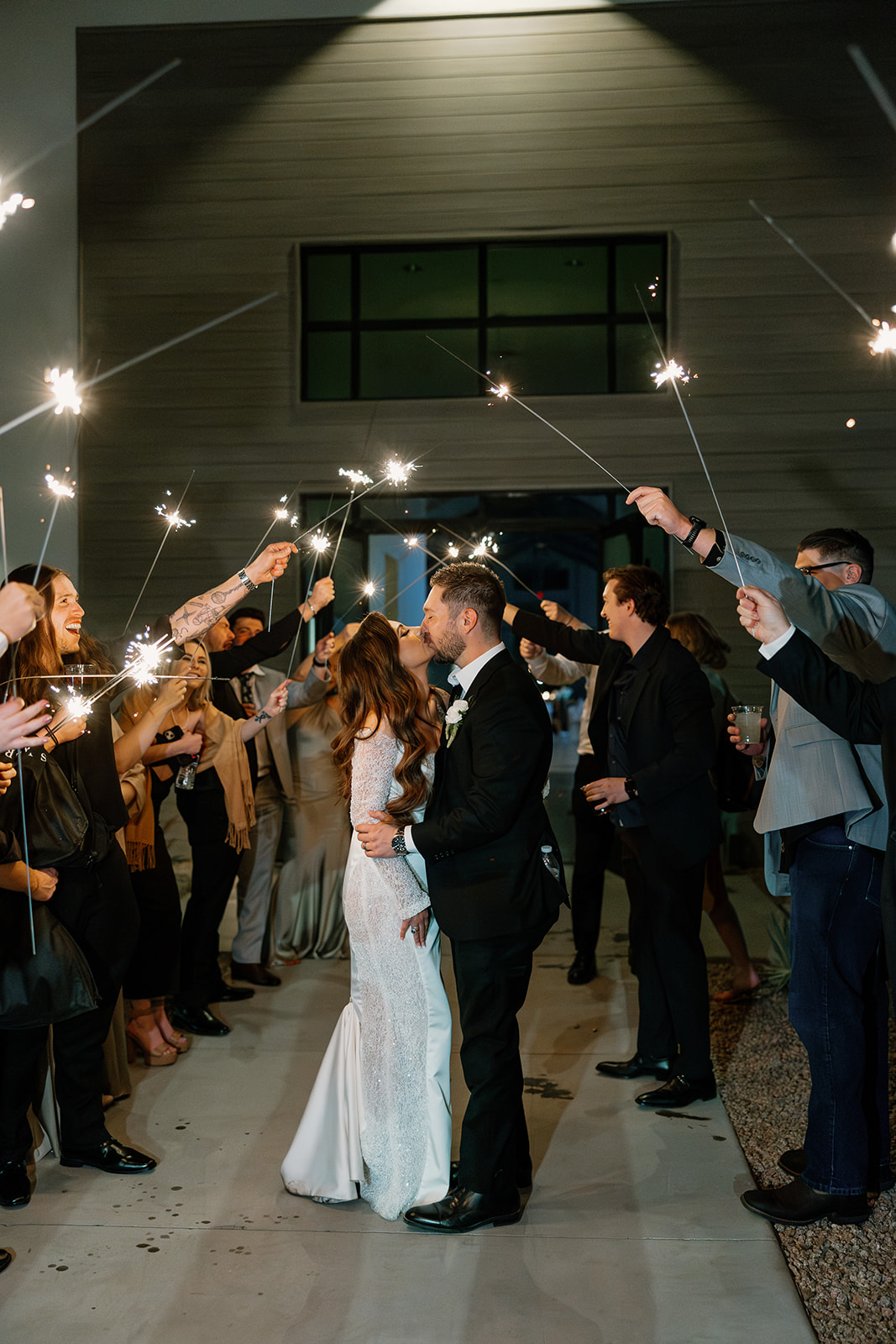 Newlyweds share a kiss under a canopy of sparklers held by cheering guests during their nighttime grand exit.