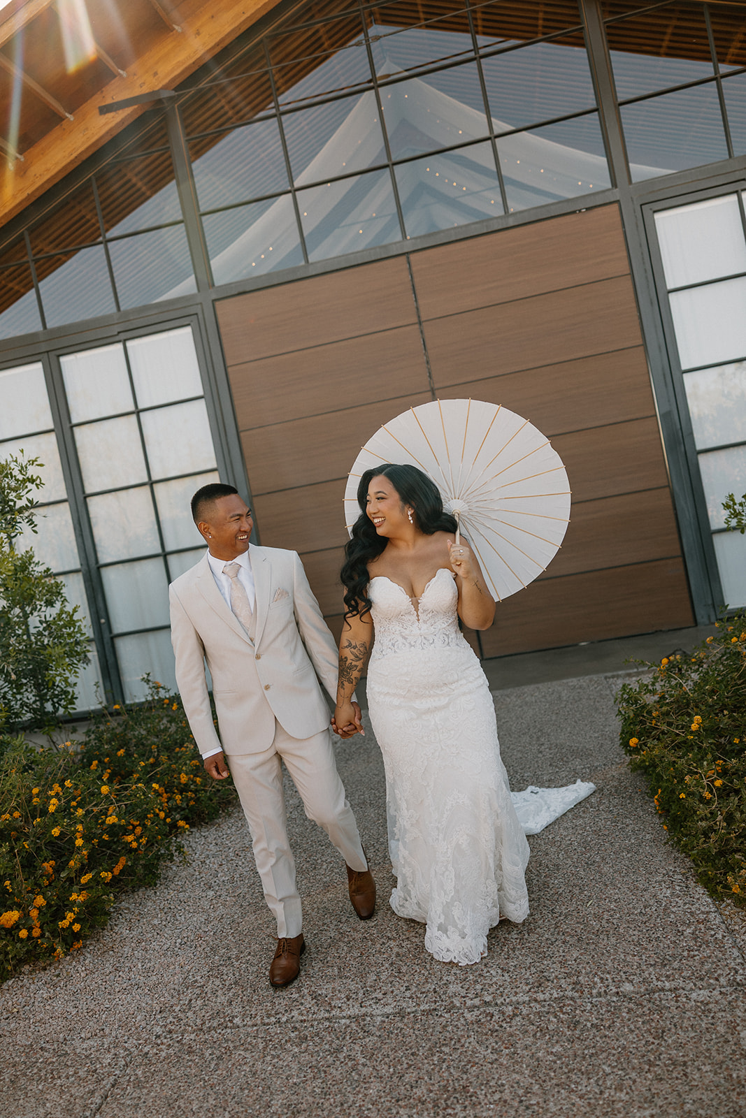 Bride and groom walking hand in hand outside the modern barn doors at The Paseo wedding venue, framed by desert blooms.