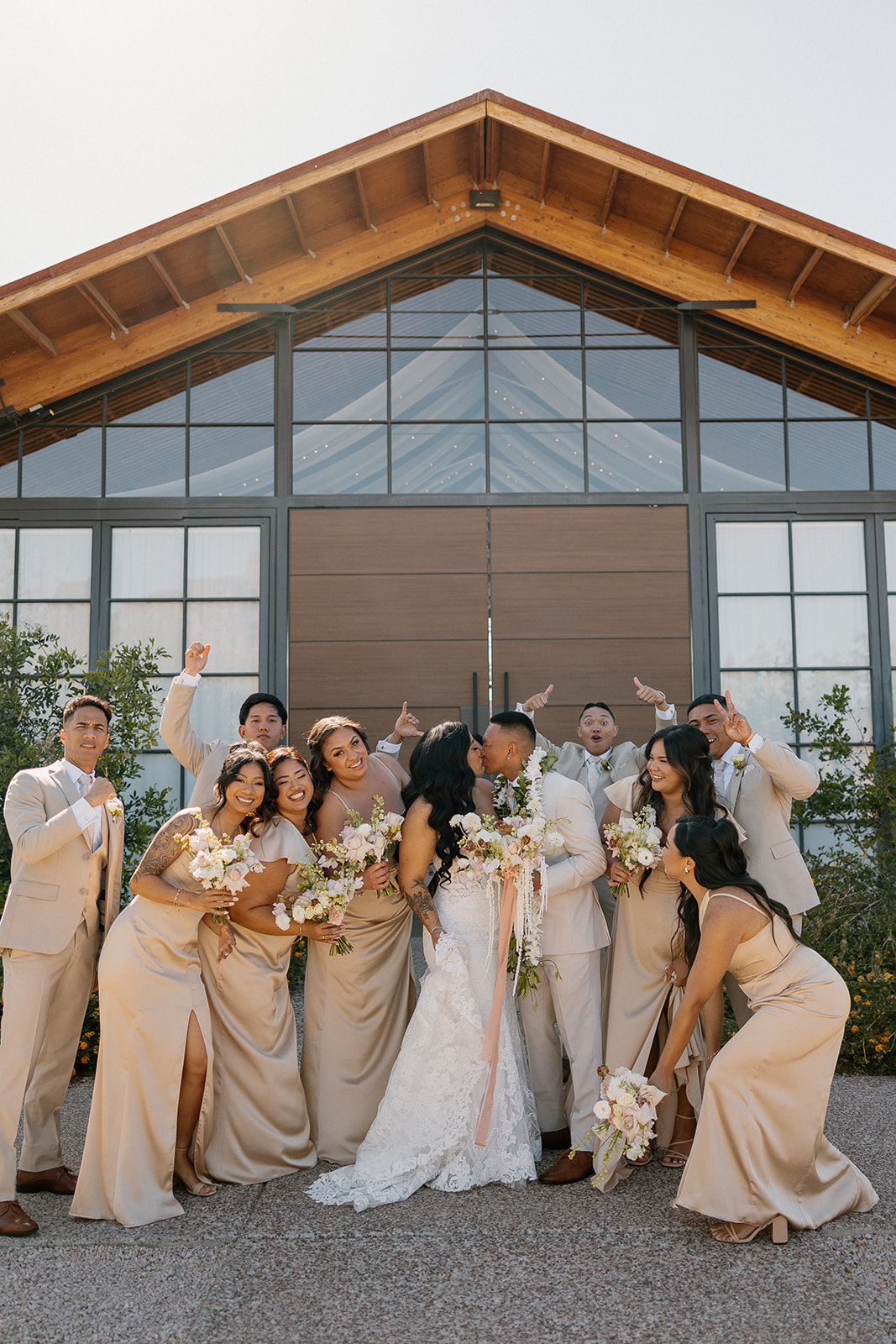 Bridal party hyping the couple with cheers and florals as they share a kiss outside The Paseo wedding venue.