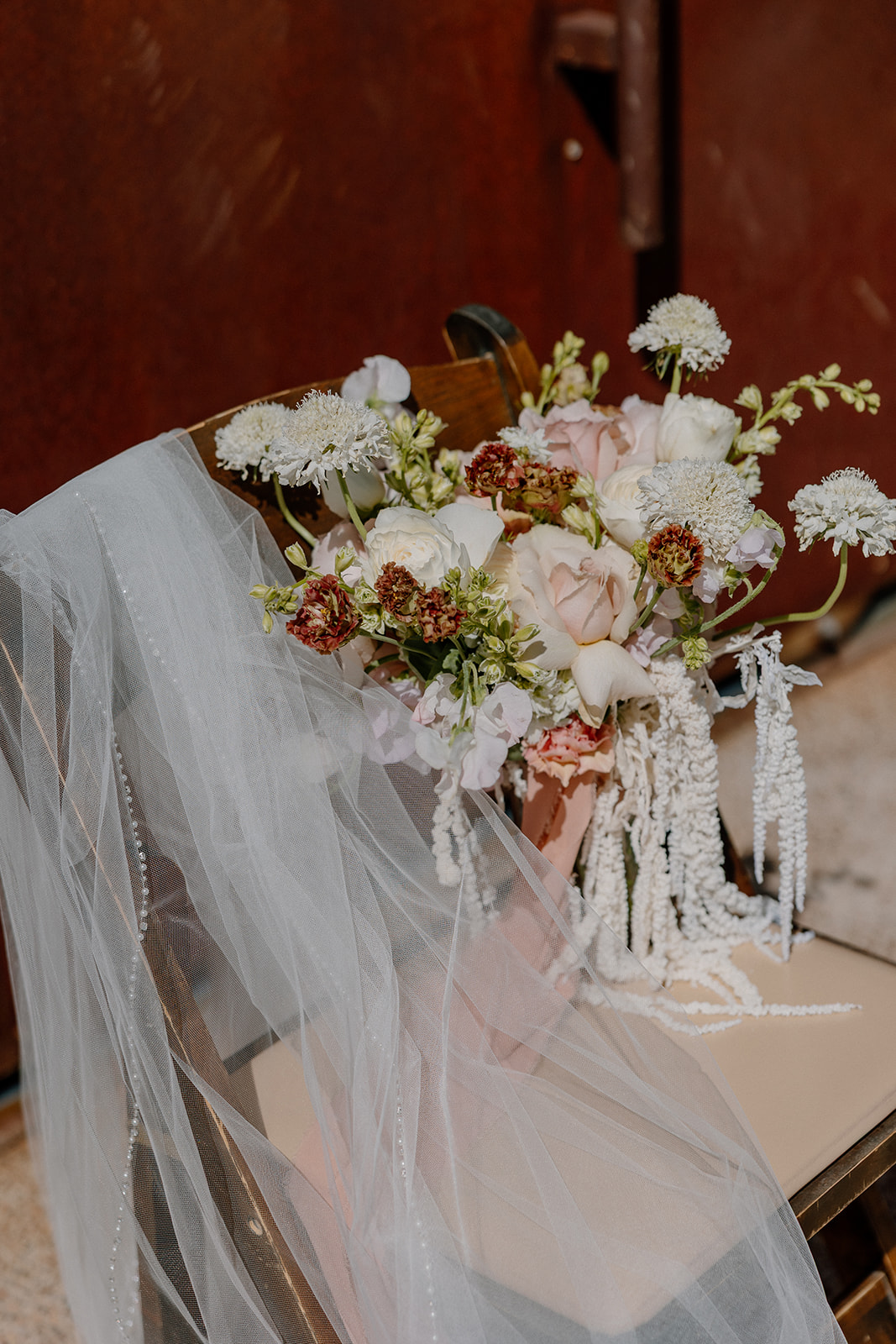 Romantic bouquet with soft desert florals and trailing ribbons resting on a ceremony chair, draped with a bridal veil.