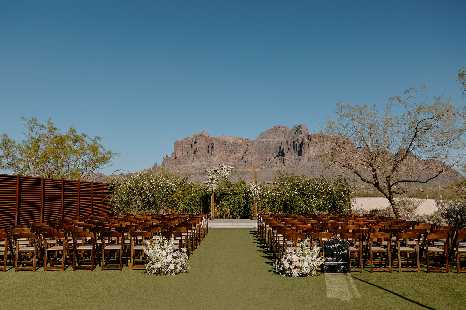 Ceremony space styled with wooden chairs, floral aisle pieces, and a stunning view of the Superstition Mountains.