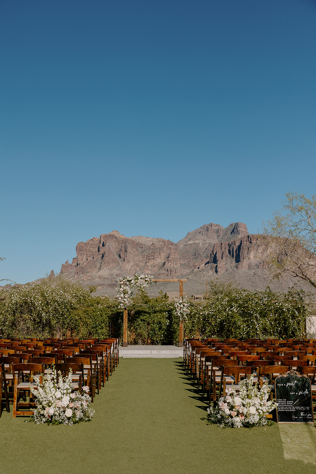 Ceremony setup under a clear blue sky with rows of wooden chairs and the Superstition Mountains in the distance.