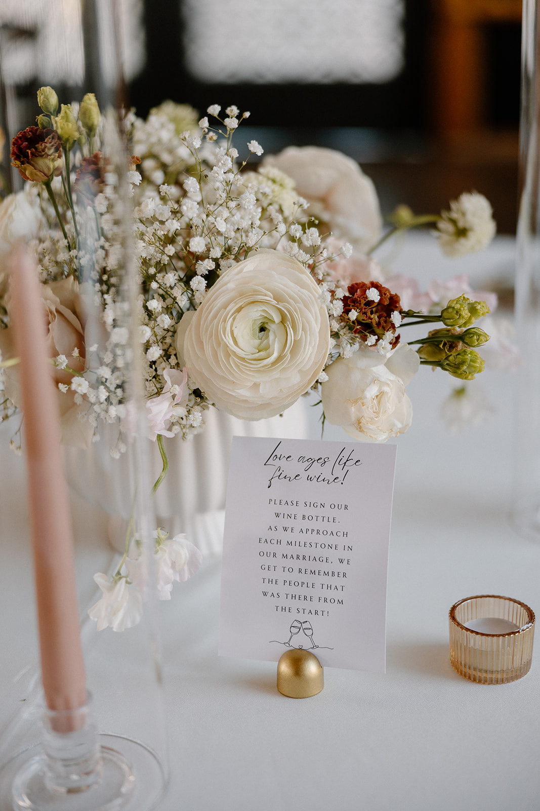 Close-up of floral centerpiece with blush taper candles and a personalized poem card, styled on a white linen table.