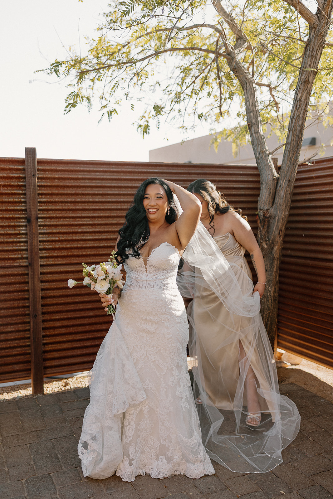 Bride laughing while adjusting her veil, with a bridesmaid behind her, getting ready for The Paseo wedding ceremony.