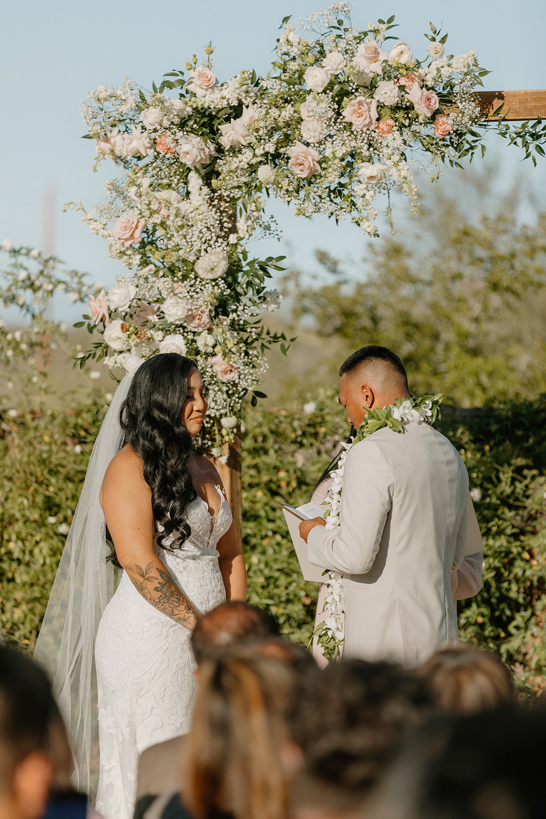 Groom reading vows to the bride during a quiet, emotional ceremony moment framed by blush florals.