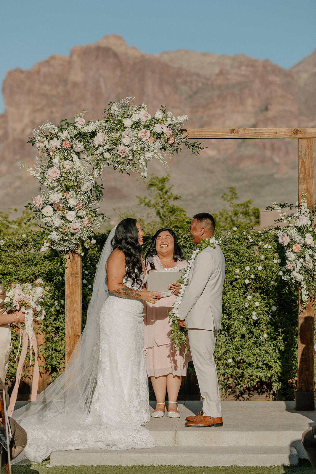 Couple holding hands under the floral ceremony arch during their The Paseo wedding, with mountains as the backdrop.