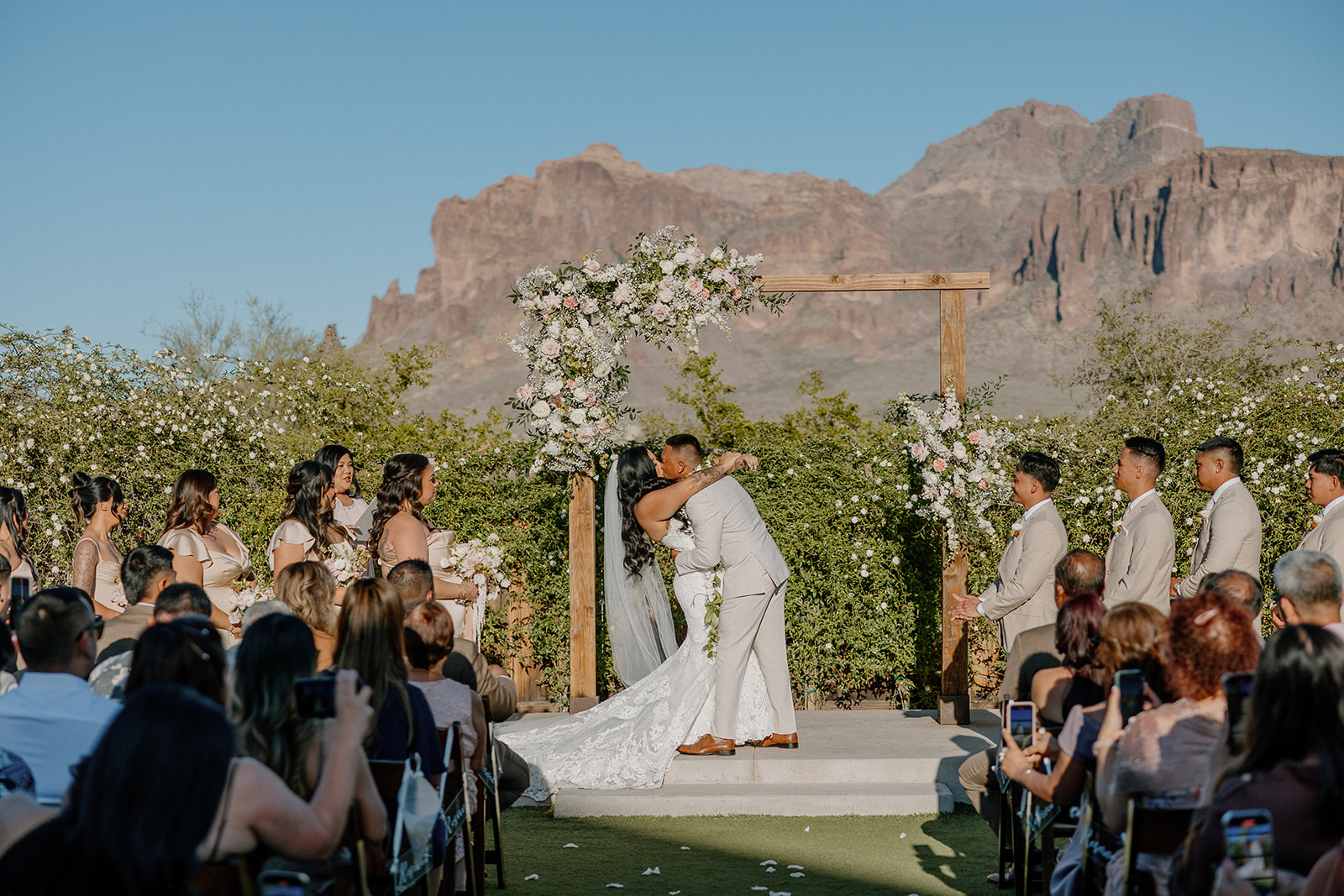 Just married kiss under the arch at The Paseo wedding, with the Superstitions glowing behind them and guests cheering.