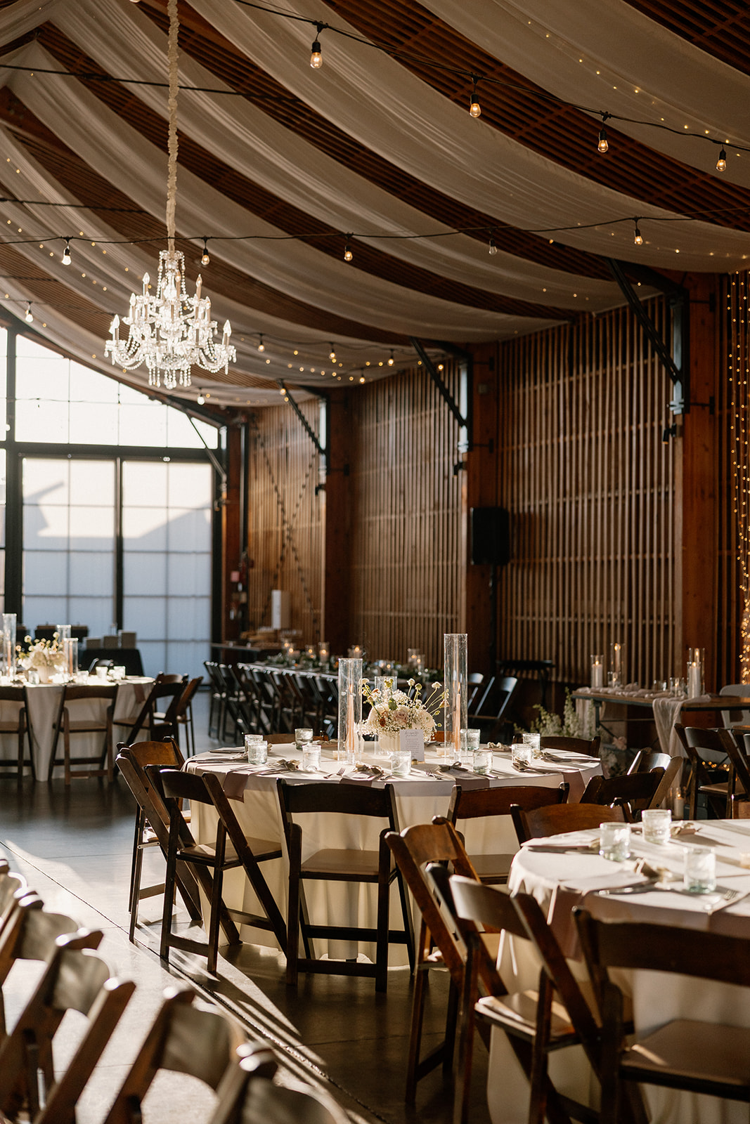 Indoor reception space with draped ceilings, candlelit tables, and golden hour light spilling through modern windows.