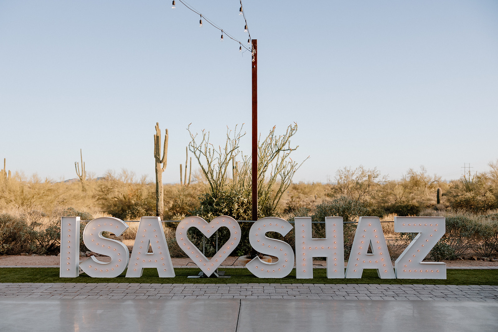 Custom marquee lights reading “ISA ❤️ SHAZ” glowing during golden hour at The Paseo wedding reception.