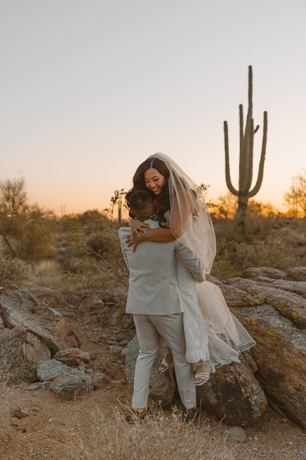 Joyful desert embrace between newlyweds during golden hour at The Paseo wedding, with cacti and glowing skies behind them.