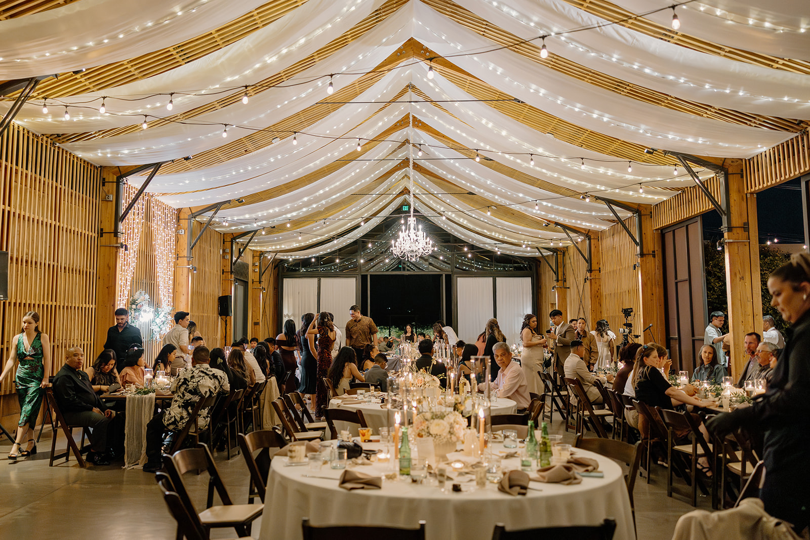 Evening reception at The Paseo wedding with twinkle lights, draped ceilings, and guests gathered around candlelit tables.