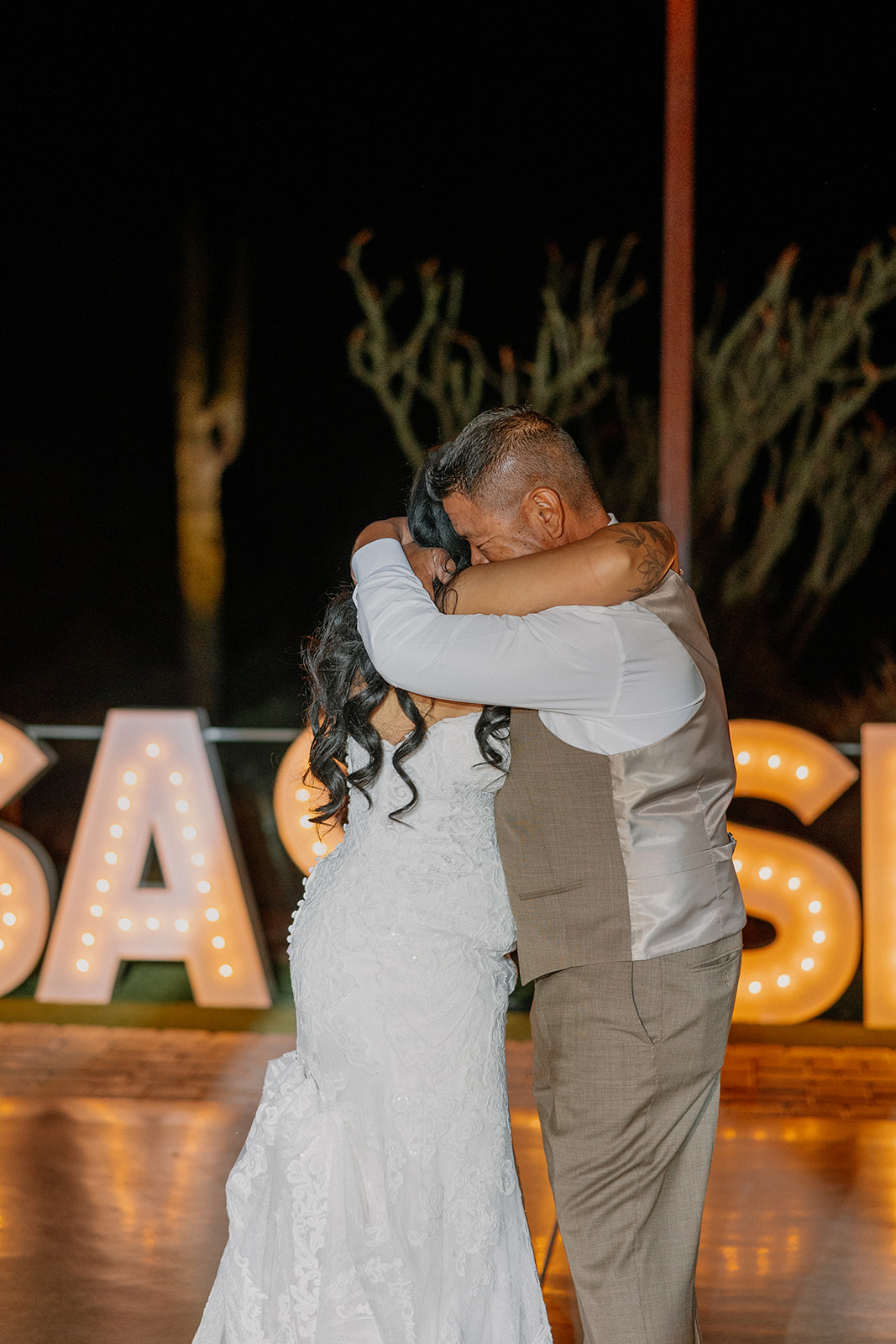 Father-daughter dance moment, emotional and quiet under glowing marquee letters on the outdoor patio.