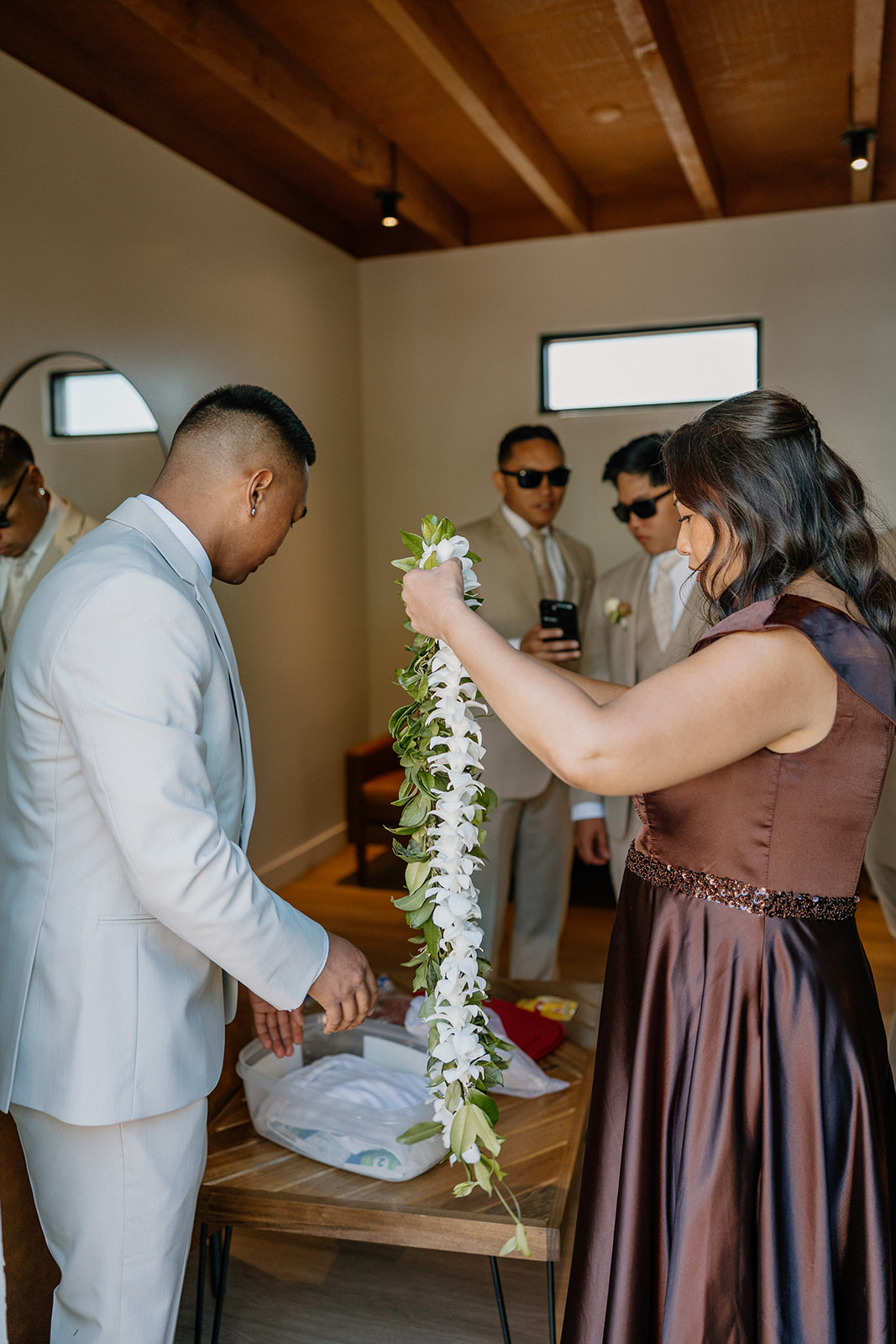 The groom receives a fresh lei from a family member, surrounded by his groomsmen before the ceremony.