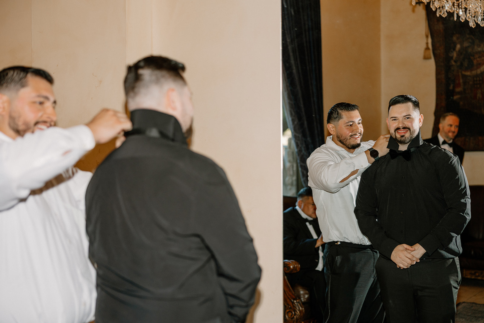 Groomsman helping the groom adjust his collar and bow tie in warm indoor light.