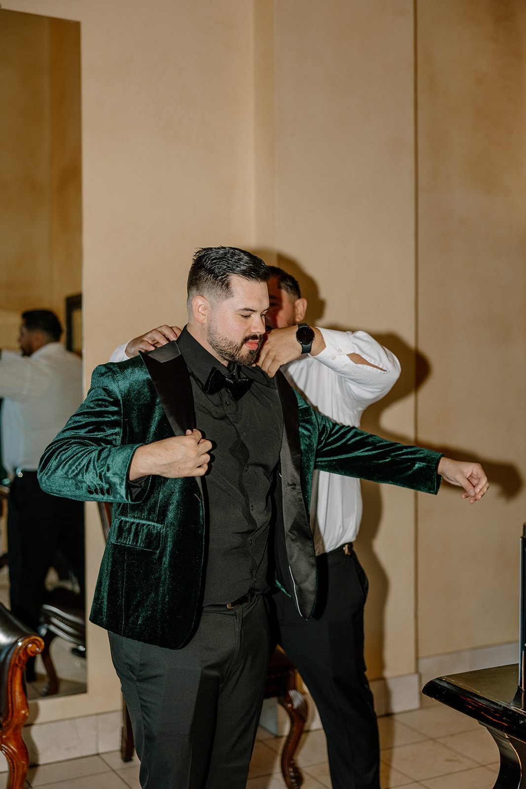Groom putting on his emerald velvet jacket with help from his groomsmen before the ceremony.