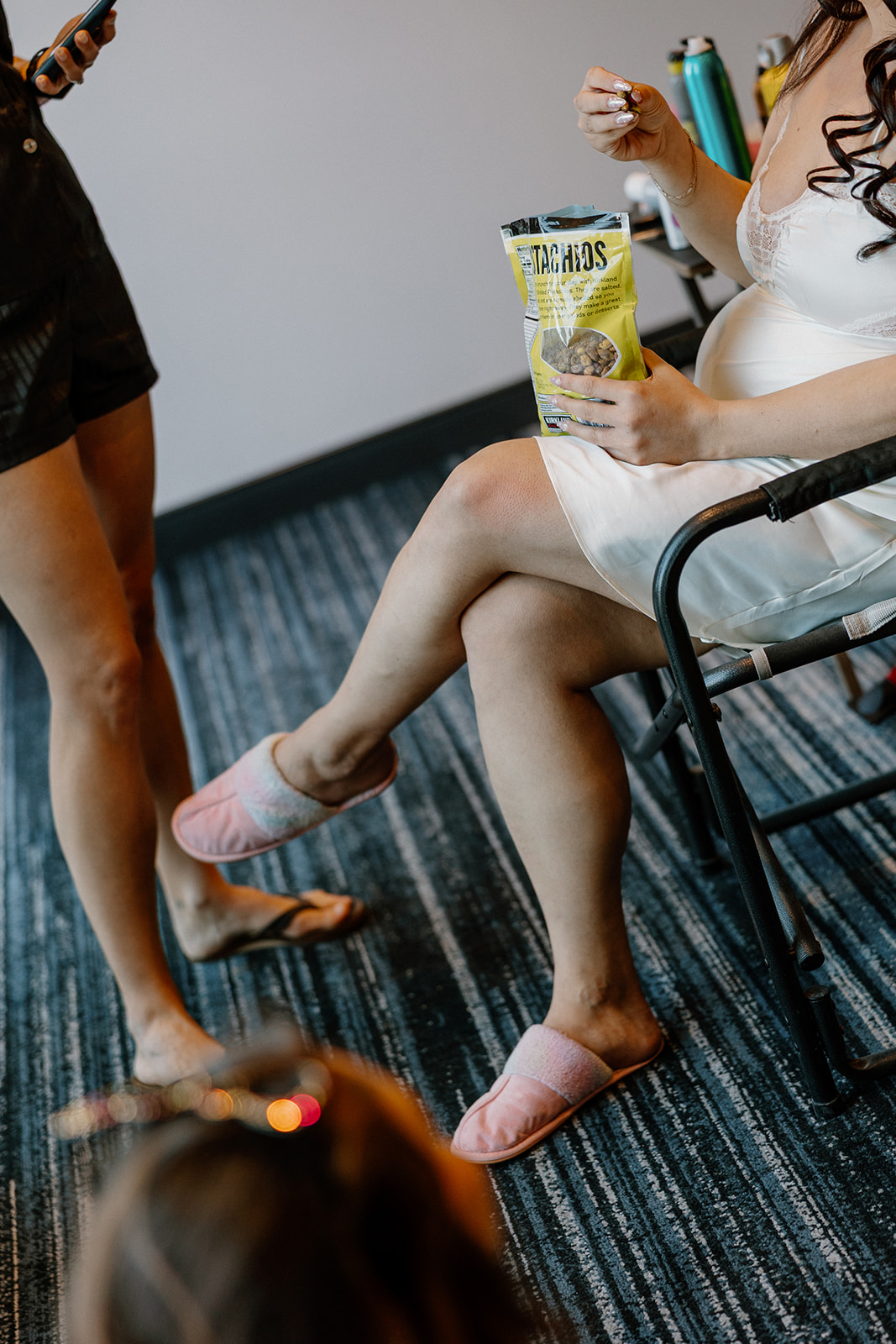 Bride in silk getting-ready outfit and pink slippers snacking and relaxing before her wedding ceremony.