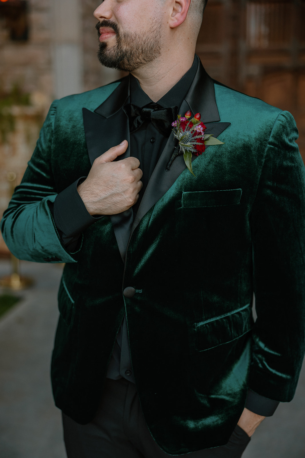 Close-up of groom adjusting his green velvet jacket with boutonniere detail.