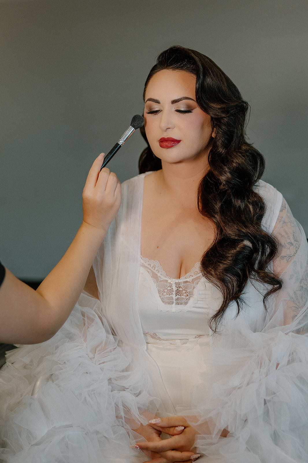 Bride with soft glam makeup and loose waves as final touches are applied before the ceremony.