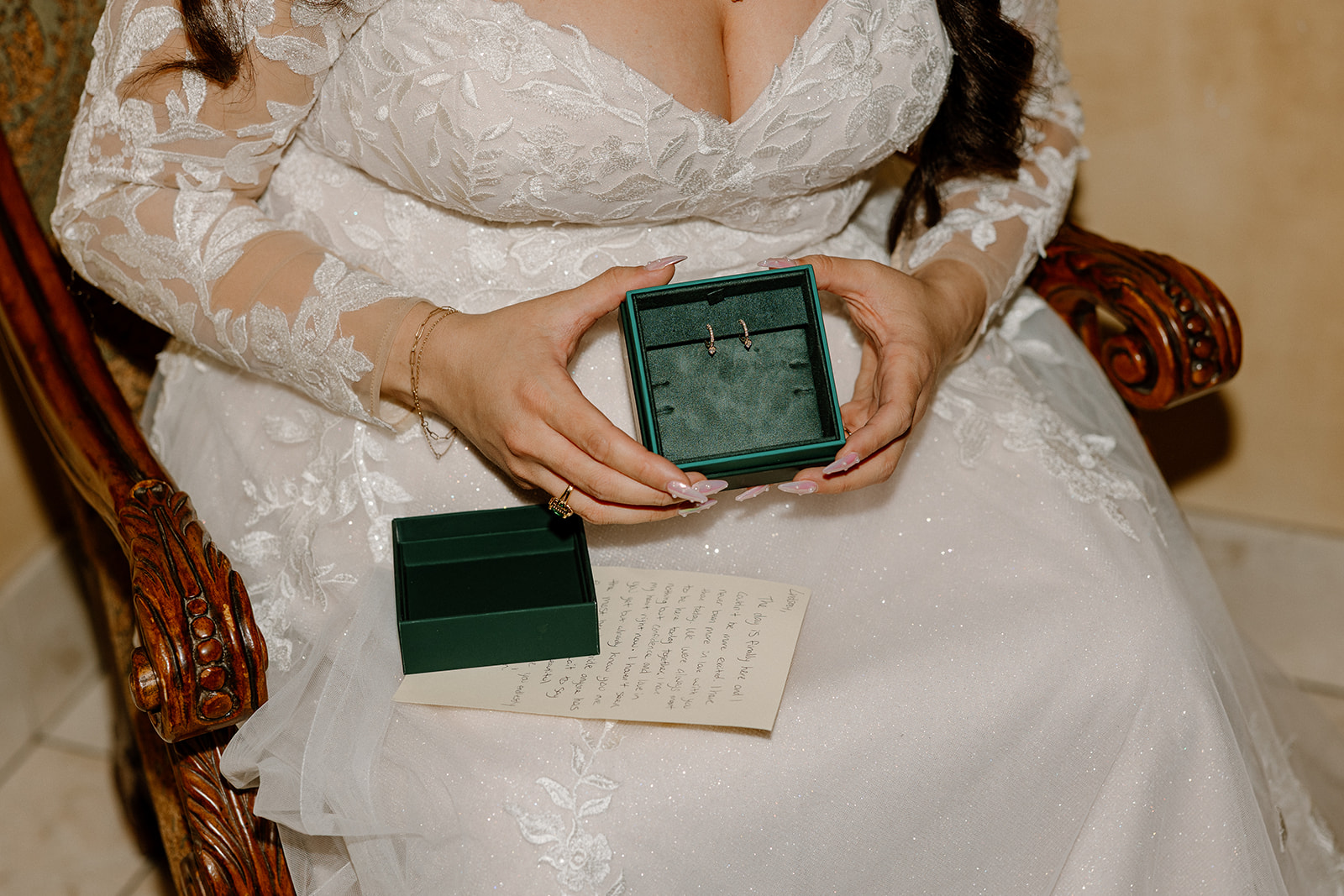 Bride holding her wedding earrings in a velvet box with handwritten note on her lap.