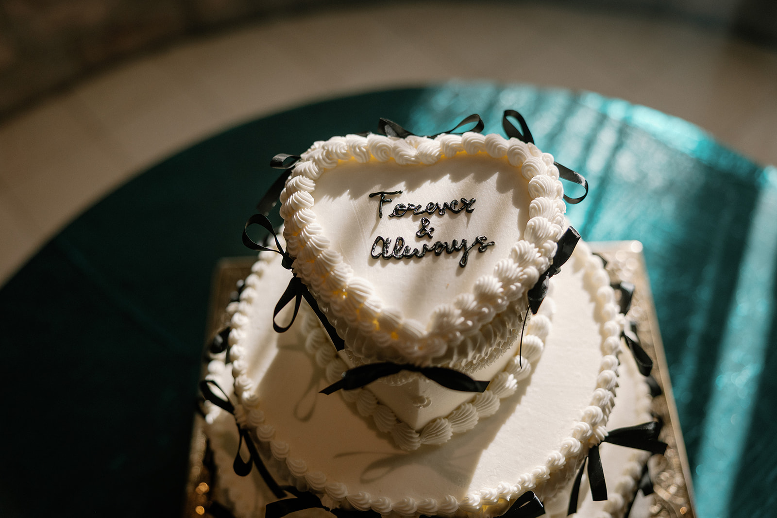 Three-tier heart-shaped wedding cake with black ribbon accents and piped frosting.