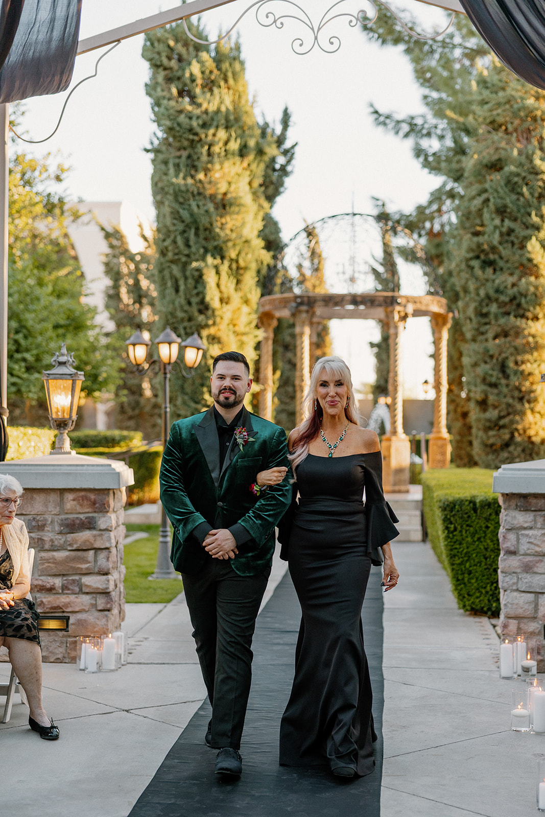 Groom walking down the aisle with his mother during the ceremony at sunset.
