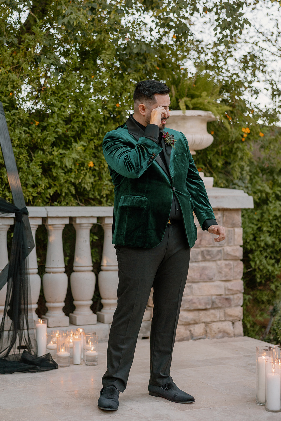 Groom wiping away tears during the ceremony surrounded by candlelight and greenery.