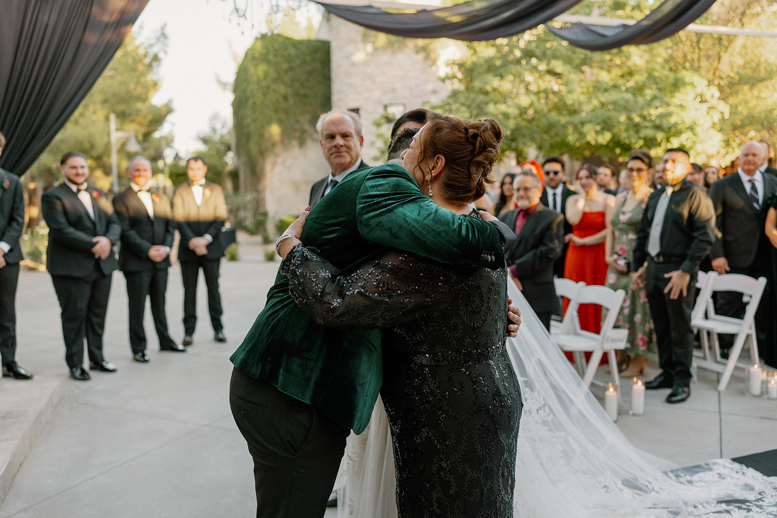 Groom hugging a family member during the ceremony while guests look on.