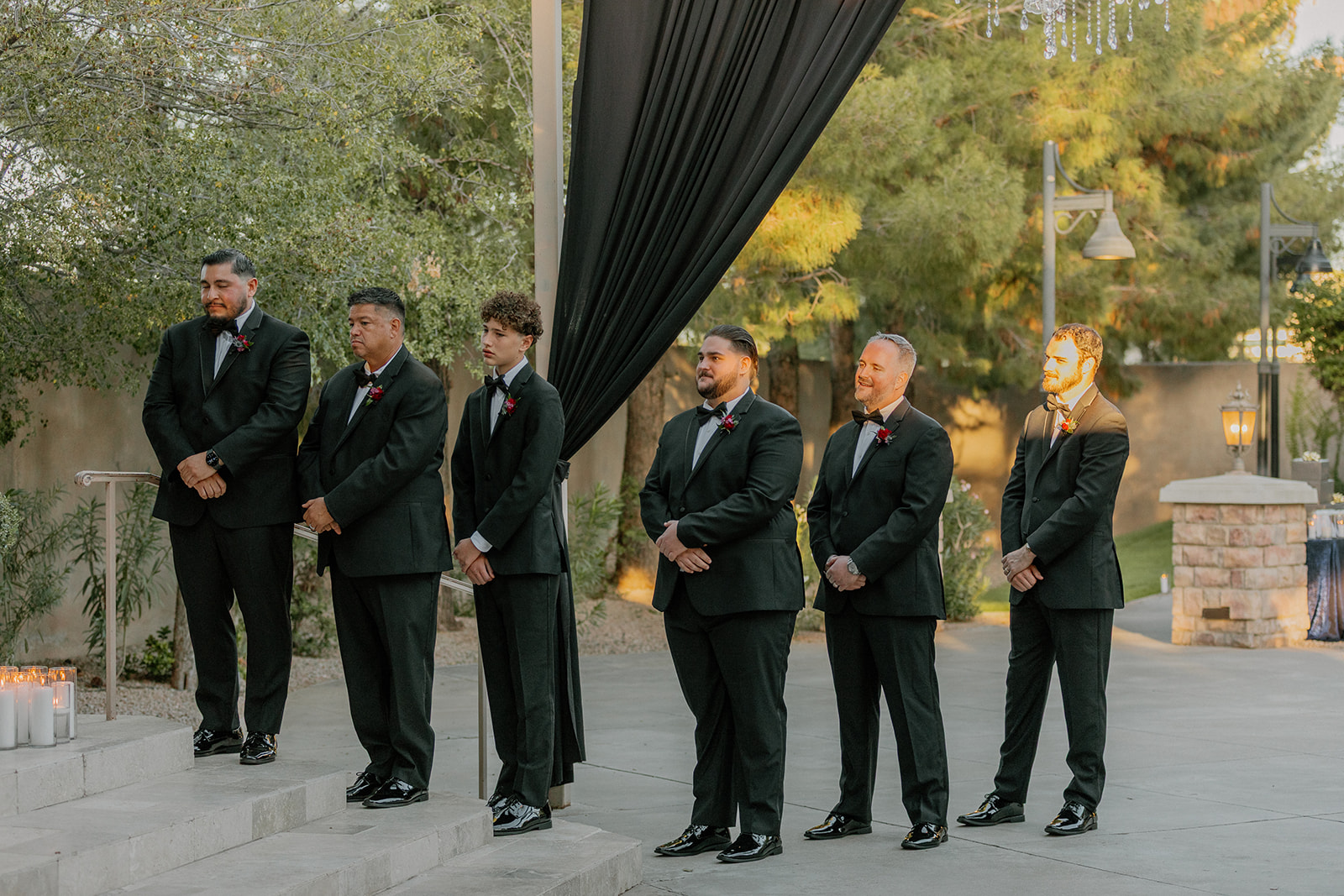 Groomsmen standing together at the front of the ceremony in black suits with red boutonnieres.