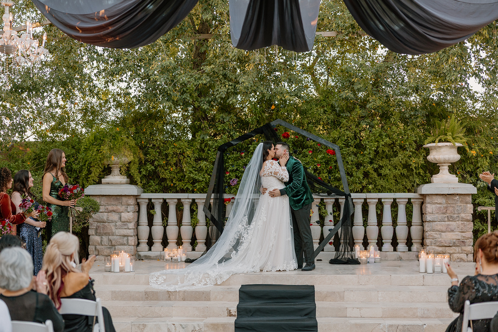 Bride and groom kissing at the altar surrounded by candles and greenery.