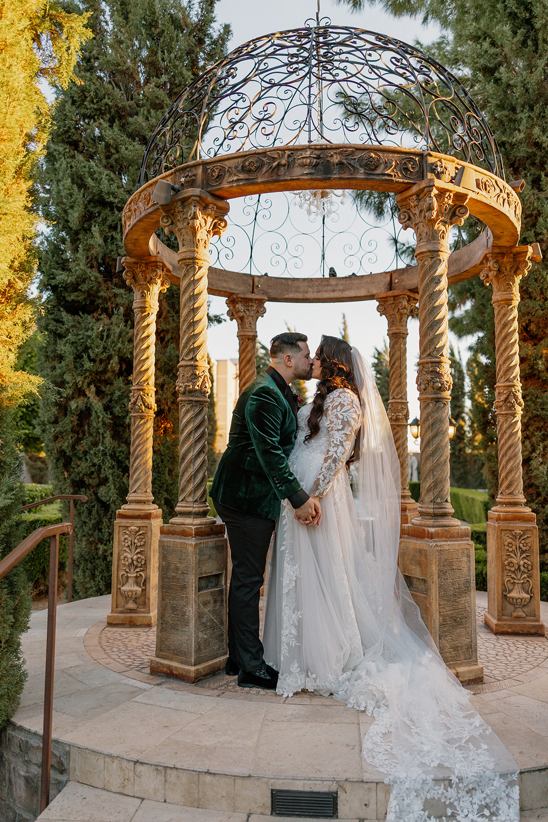 Bride and groom kissing beneath ornate stone columns during golden hour at this wedding venue in Chandler.