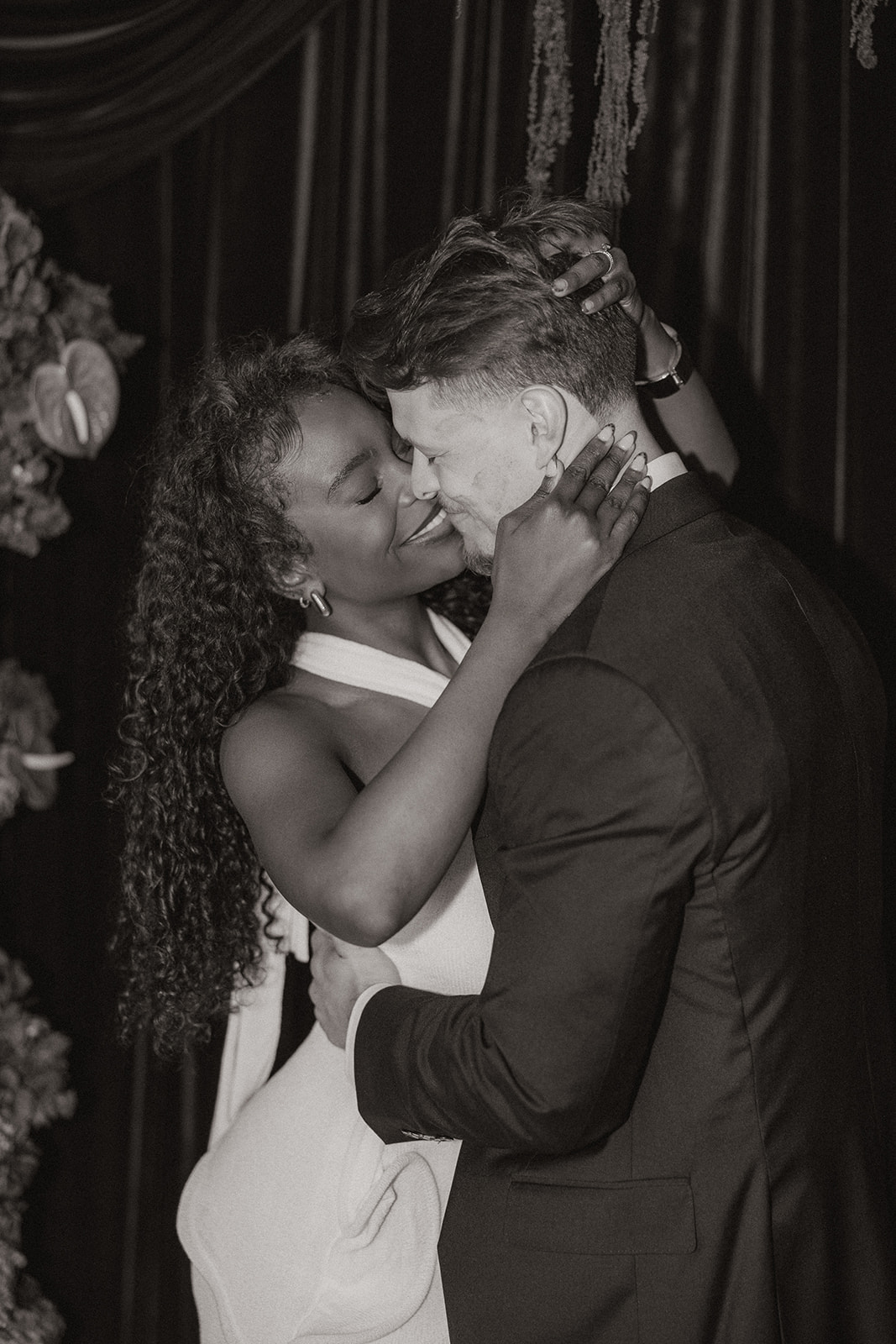 Black and white close-up of the couple embracing with foreheads nearly touching, her hands resting at his jaw and neck, creating an intimate moment during their editorial engagement photos session.