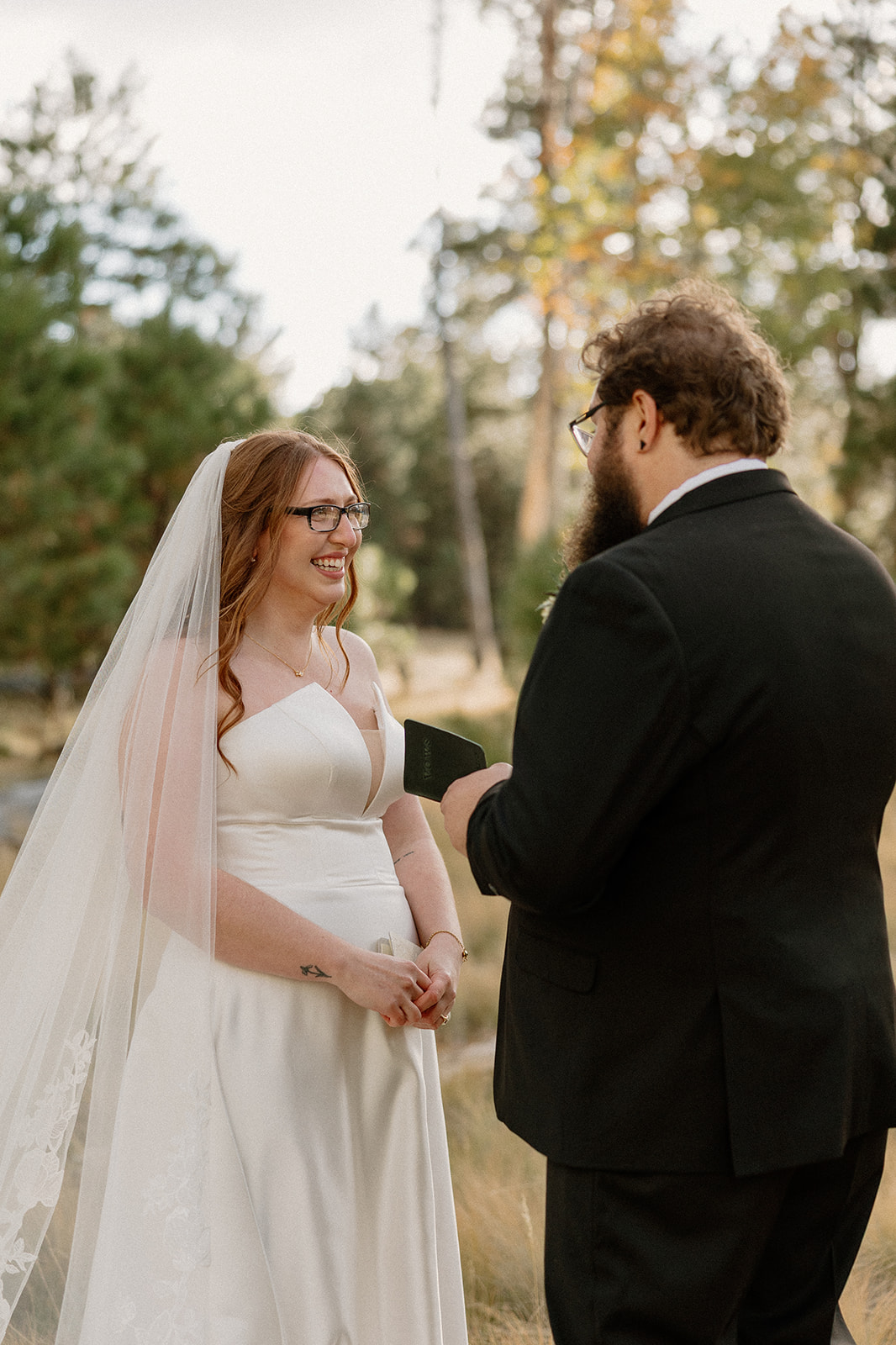 Bride smiling while reading handwritten vows during an intimate forest ceremony.