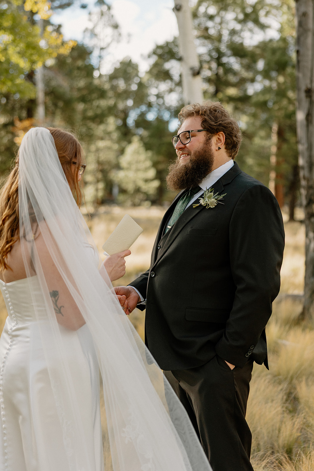 Groom smiling as he listens to vows in a quiet wooded setting.