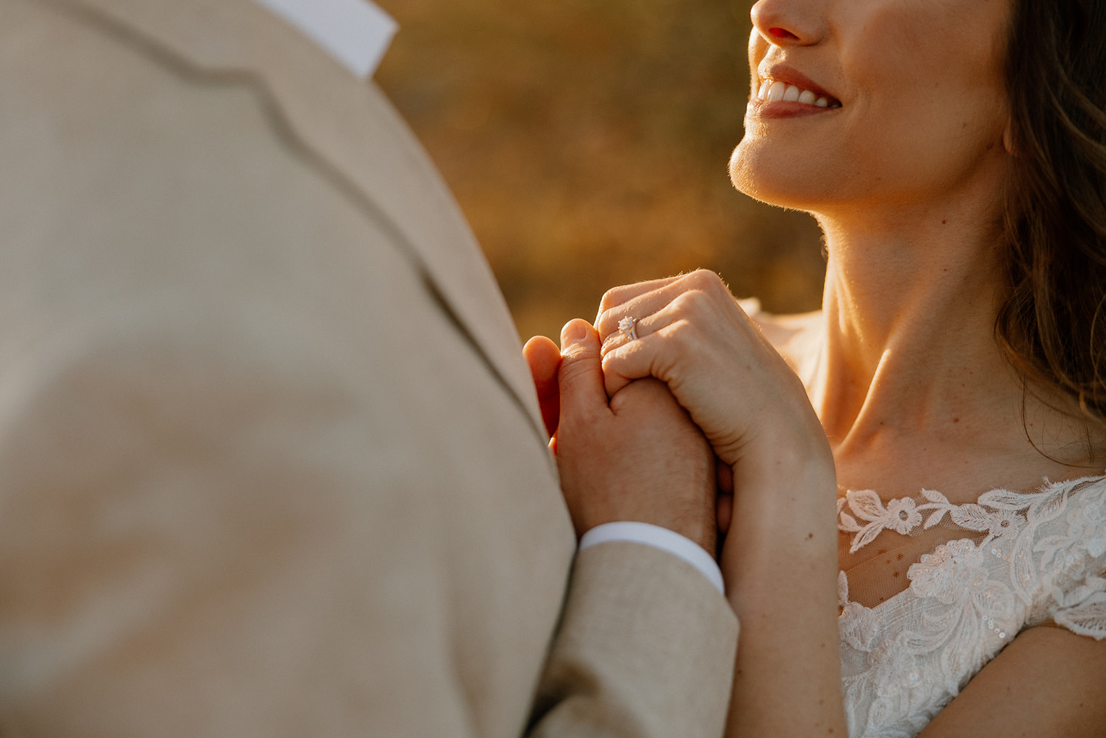 Bride holding groom’s hands during vows with soft sunset light on her engagement ring.