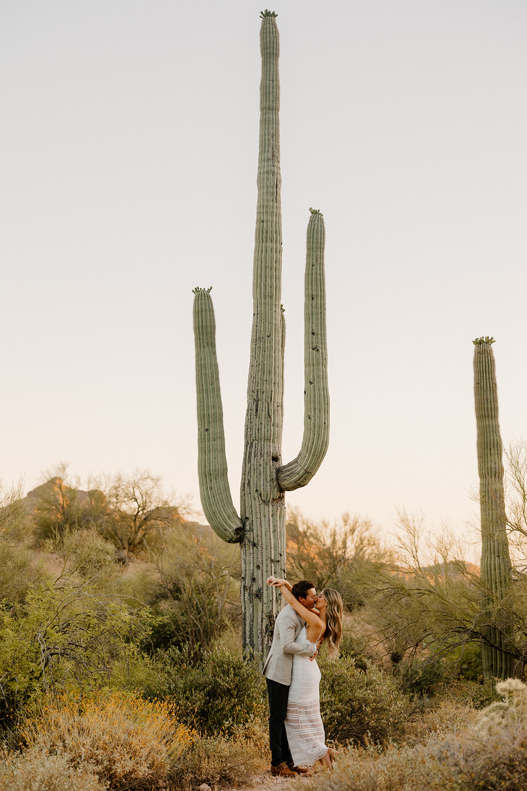Couple embracing beneath tall saguaro cacti in the Arizona desert.