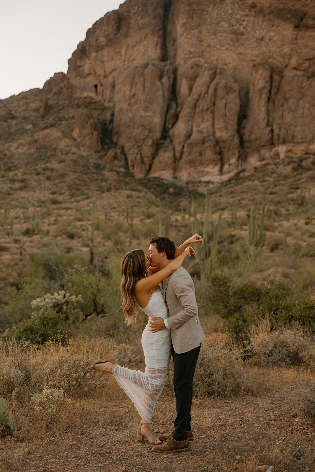 Bride jumping into groom’s arms in a desert landscape surrounded by cacti and mountains.