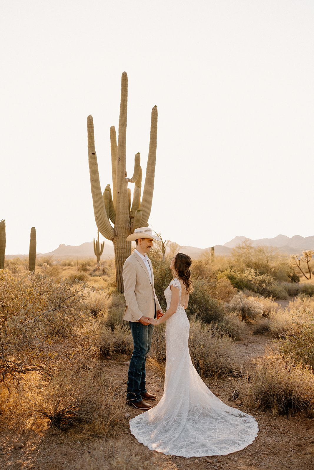 Bride and groom holding hands beneath towering saguaro cacti as they elope in Arizona.
