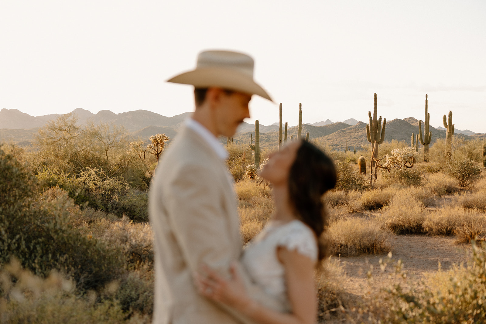 Couple embracing in a cactus-filled desert landscape at golden hour.